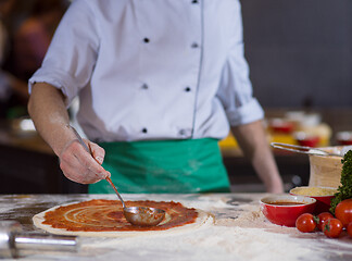 Image showing Chef smearing pizza dough with ketchup