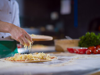 Image showing chef sprinkling cheese over fresh pizza dough