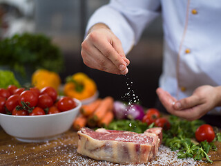 Image showing Chef putting salt on juicy slice of raw steak