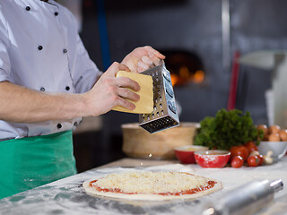 Image showing chef sprinkling cheese over fresh pizza dough