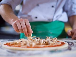 Image showing chef putting fresh mushrooms on pizza dough