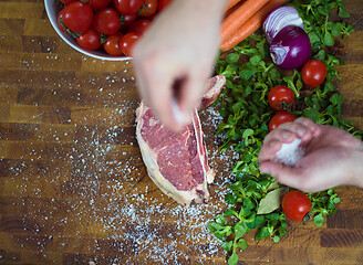 Image showing Chef putting salt on juicy slice of raw steak