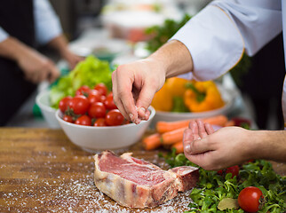 Image showing Chef putting salt on juicy slice of raw steak