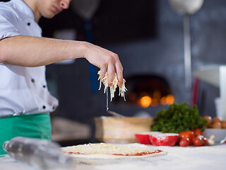 Image showing chef sprinkling cheese over fresh pizza dough