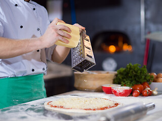 Image showing chef sprinkling cheese over fresh pizza dough