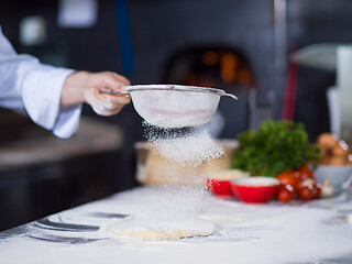 Image showing chef sprinkling flour over fresh pizza dough