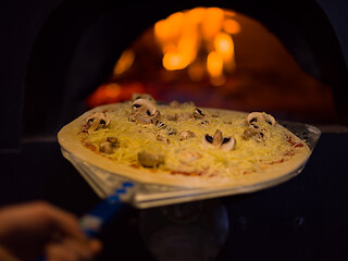 Image showing chef putting delicious pizza to brick wood oven