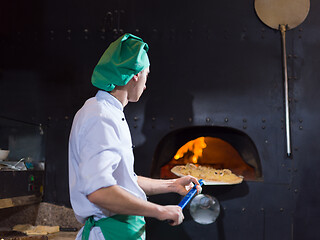 Image showing chef putting delicious pizza to brick wood oven