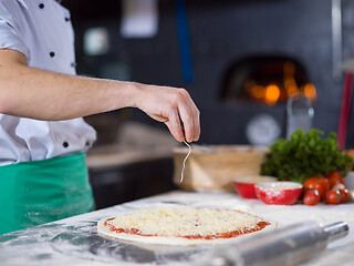 Image showing chef sprinkling cheese over fresh pizza dough