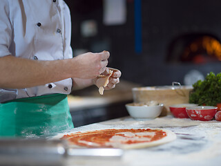 Image showing chef putting cut sausage or ham on pizza dough