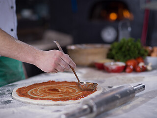 Image showing Chef smearing pizza dough with ketchup