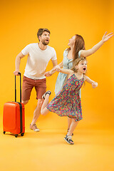 Image showing Happy parents with daughter and suitcase at studio isolated on yellow background