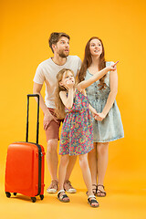 Image showing Happy parents with daughter and suitcase at studio isolated on yellow background