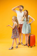 Image showing Happy parents with daughter and suitcase at studio isolated on yellow background