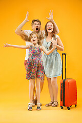 Image showing Happy parents with daughter and suitcase at studio isolated on yellow background