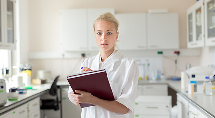 Image showing Portrait of young, confident female health care professional taking notes during inventory in scientific laboratory or medical doctors office