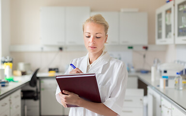 Image showing Portrait of young, confident female health care professional taking notes during inventory in scientific laboratory or medical doctors office