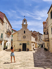 Image showing Female tourist taking photo of mall church on square of small urban village of Stari grad on Hvar island in Croatia, Adriatic Sea, Europe