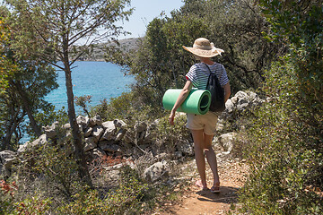 Image showing Young active feamle tourist wearing small backpack walking on coastal path among pine trees looking for remote cove to swim alone in peace on seaside in Croatia. Travel and adventure concept