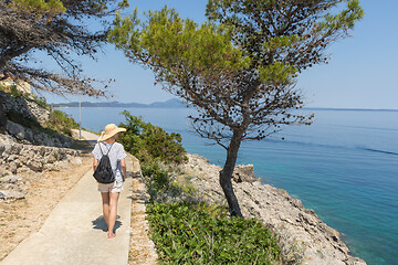 Image showing Young active feamle tourist wearing small backpack walking on coastal path among pine trees looking for remote cove to swim alone in peace on seaside in Croatia. Travel and adventure concept