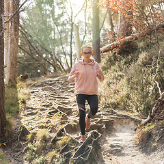 Image showing Active sporty woman listening to the music while running in autumn fall forest. Female runner training outdoor. Healthy lifestyle image of young caucasian woman jogging outside