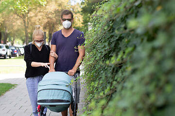 Image showing Worried young parent walking on empty street with stroller wearing medical masks to protect them from corona virus. Social distancing life during corona virus pandemic