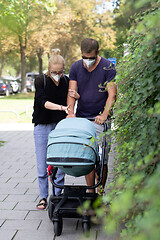 Image showing Worried young parent walking on empty street with stroller wearing medical masks to protect them from corona virus. Social distancing life during corona virus pandemic