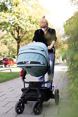 Image showing Worried young mom walking on empty street with stroller wearing medical masks to protect her from corona virus. Social distancing life during corona virus pandemic