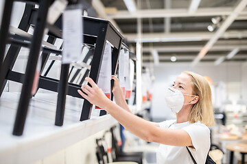 Image showing New normal during covid epidemic. Caucasian woman shopping at retail furniture and home accessories store wearing protective medical face mask to prevent spreading of corona virus