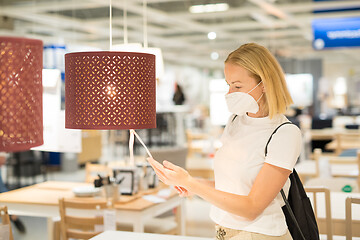 Image showing New normal during covid epidemic. Caucasian woman shopping at retail furniture and home accessories store wearing protective medical face mask to prevent spreading of corona virus