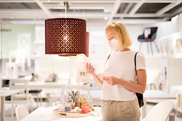 Image showing New normal during covid epidemic. Caucasian woman shopping at retail furniture and home accessories store wearing protective medical face mask to prevent spreading of corona virus