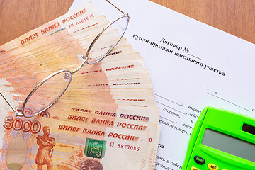 Image showing On the table there is a contract for the sale of a land plot, a bundle of money, a calculator and glasses