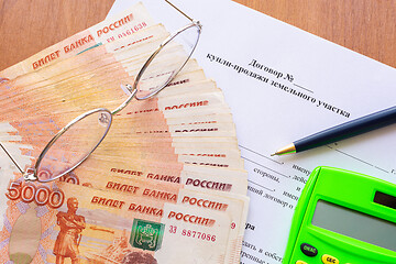 Image showing On the table is a contract for the sale of a land plot, a bundle of money, a calculator, glasses and a pen