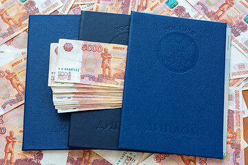 Image showing Three blue higher education diplomas lie in the background from the money, a bundle of money sticks out between the diplomas