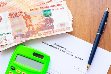 Image showing On the table is a contract for the sale of a land plot, a bundle of money, a calculator and a pen