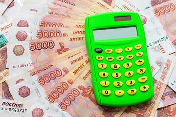 Image showing A green calculator lies on a stack of five thousandth bills spread out in a fan.