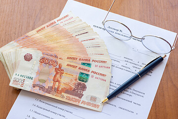 Image showing On the table is a contract for the sale of a land plot, a bundle of money, a pen and glasses