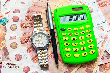 Image showing Against the background of Russian five-thousandth bills lies a calculator with the number one million, a watch and a pen