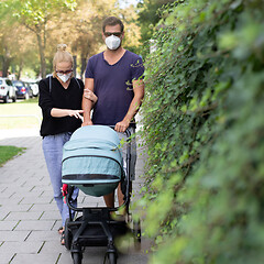 Image showing Worried young parent walking on empty street with stroller wearing medical masks to protect them from corona virus. Social distancing life during corona virus pandemic