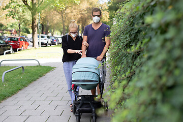 Image showing Worried young parent walking on empty street with stroller wearing medical masks to protect them from corona virus. Social distancing life during corona virus pandemic