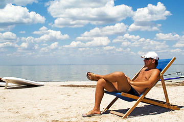 Image showing Young man on a chair on a beach against a gulf and clouds