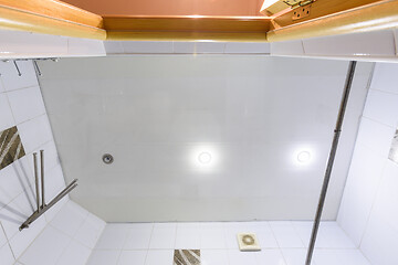 Image showing A fragment of a bathroom interior, a view of the ceiling made of plastic panels with three lamps, one light bulb burned out