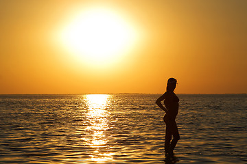 Image showing Silhouette of the young woman on a sea bay on a sunset