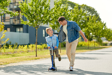 Image showing happy father and little son riding scooter in city