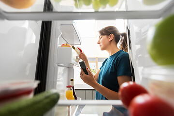 Image showing woman with smartphone makes list of food in fridge