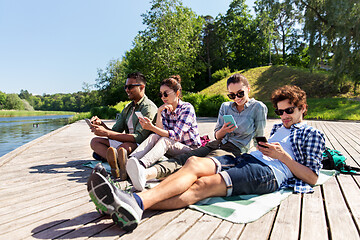 Image showing friends with smartphone on lake pier in summer