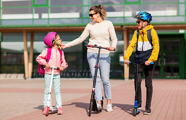 Image showing happy school children with mother riding scooters