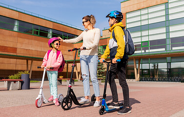 Image showing happy school children with mother riding scooters