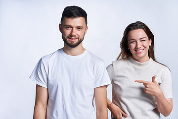 Image showing Smiling couple standing over light background, joyful female pointing at guy and winking