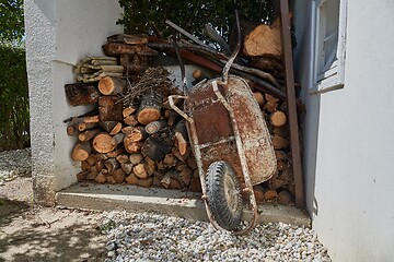 Image showing Wheel barrow in the garden by the pile of logs